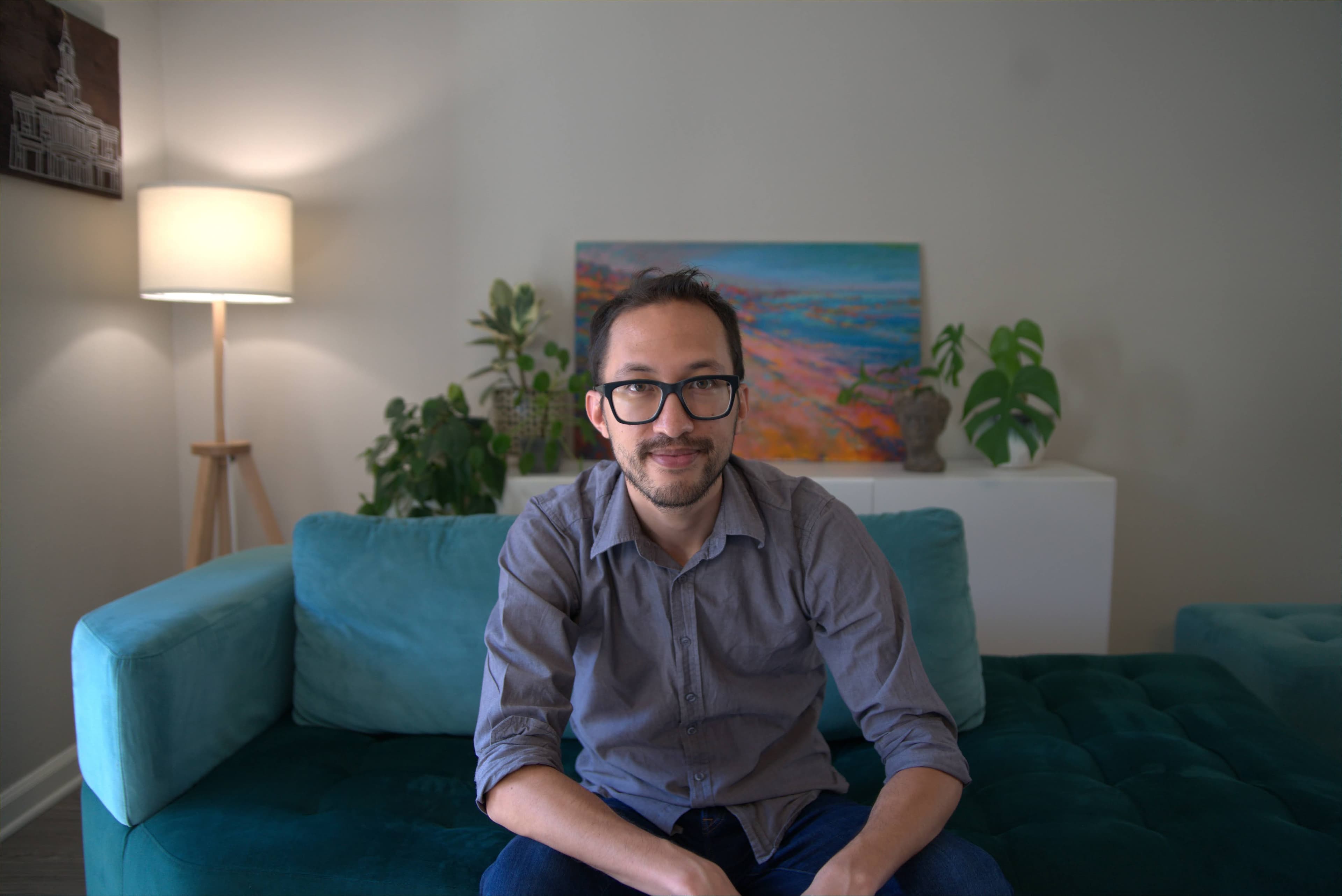 Daniel Nash seated on a teal sofa, smiling toward the camera.