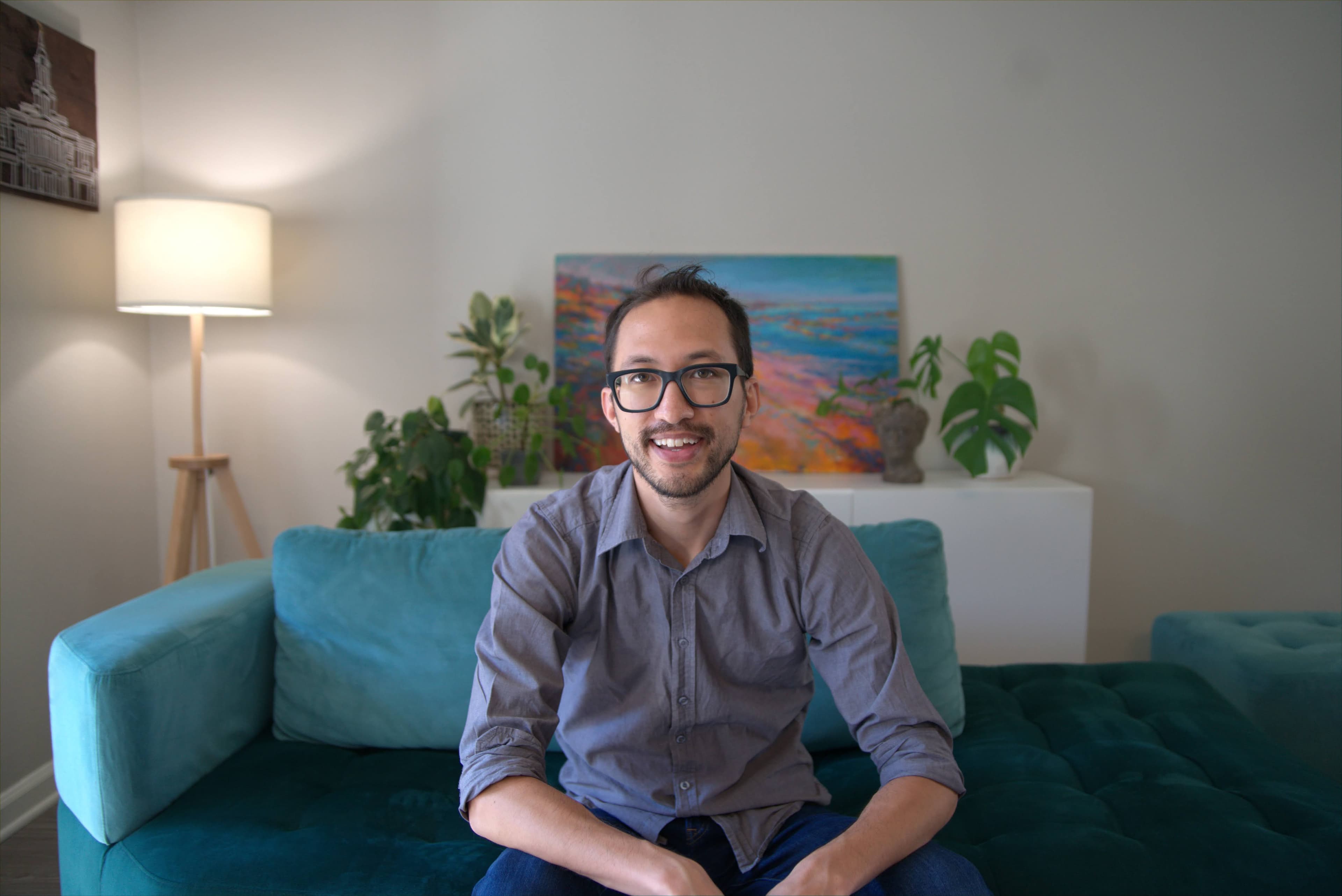 Daniel Nash facing forward on a teal sofa with artwork behind.